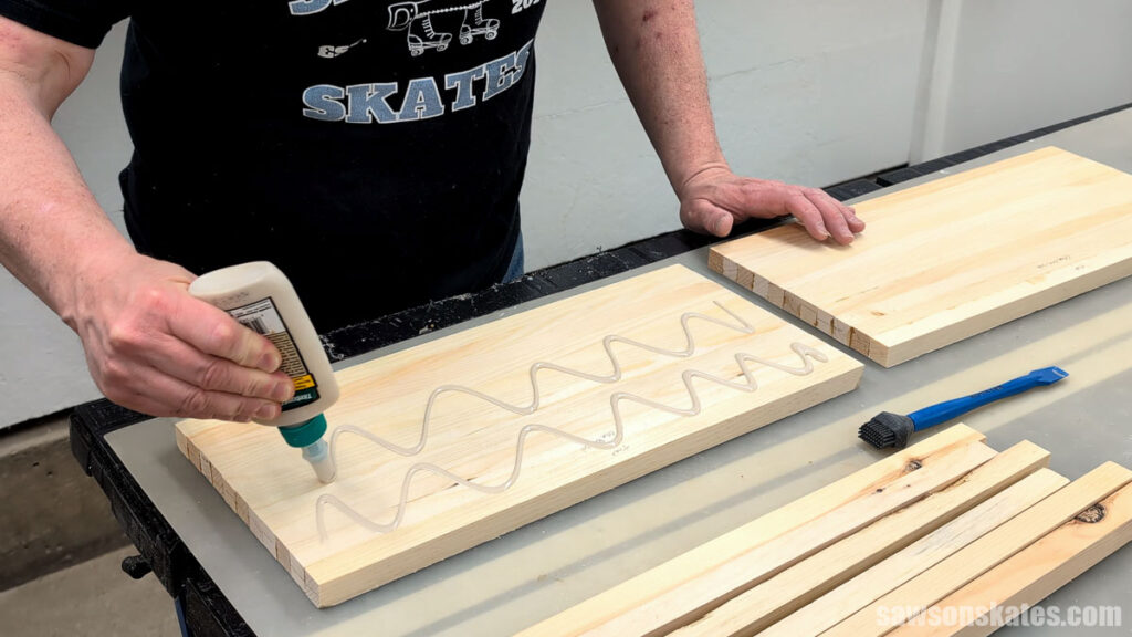 Person applying wood glue in a wavy pattern to a glued-up wood panel.
