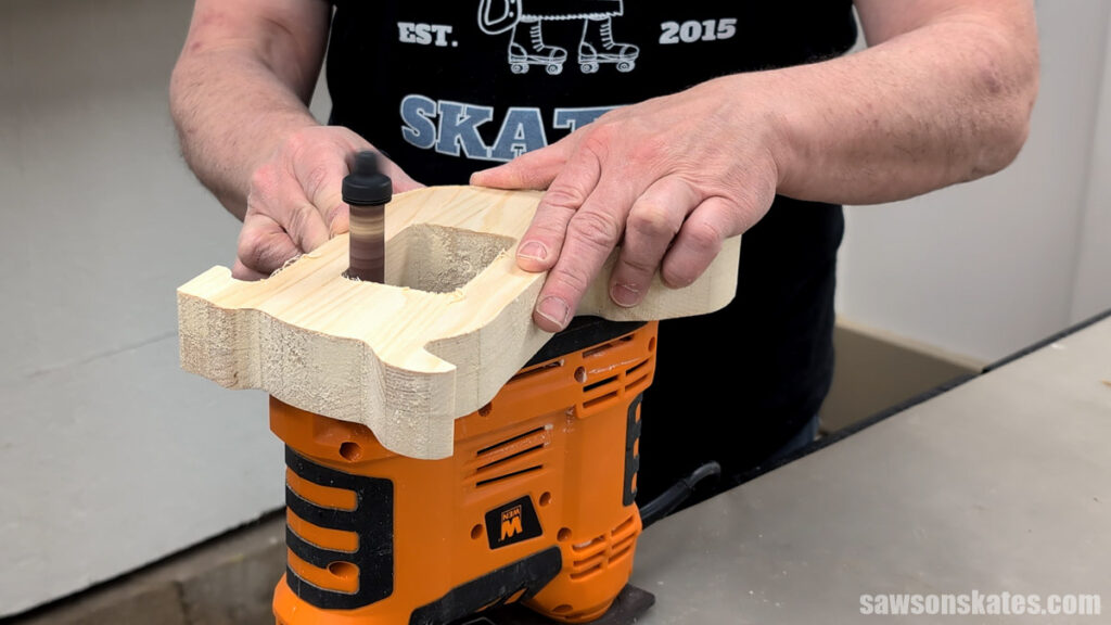 Person using a portable spindle sander to smooth the edges of a wooden dog shape.