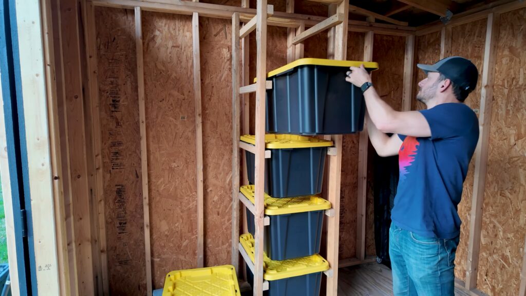 Person sliding a plastic storage tote into a tall wooden rack.