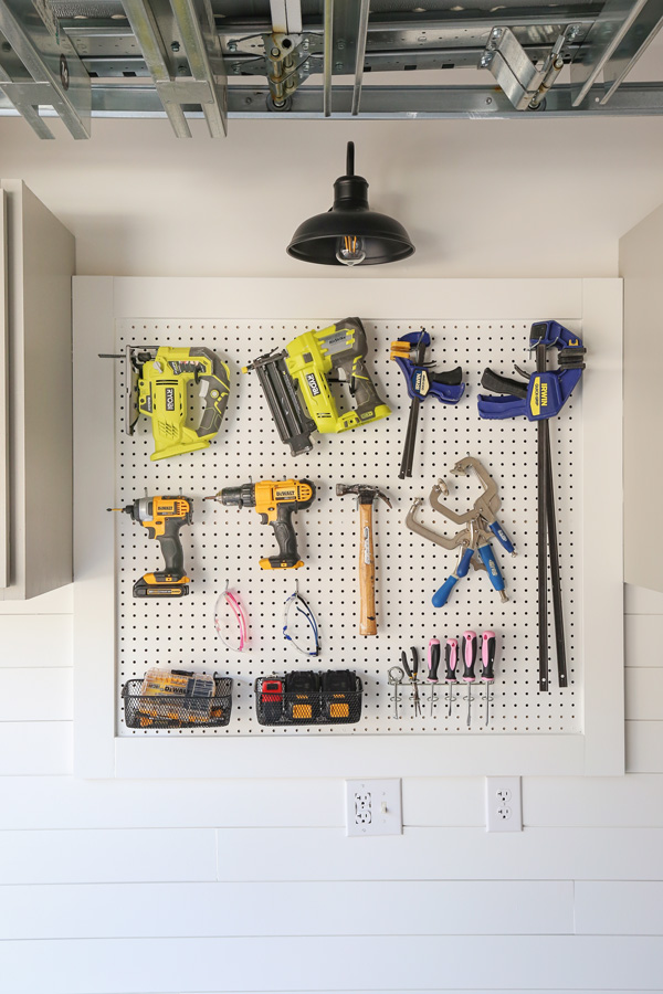 Pegboard tool wall with drills, nailers, clamps, screwdrivers, and small storage baskets hanging in a garage workshop.