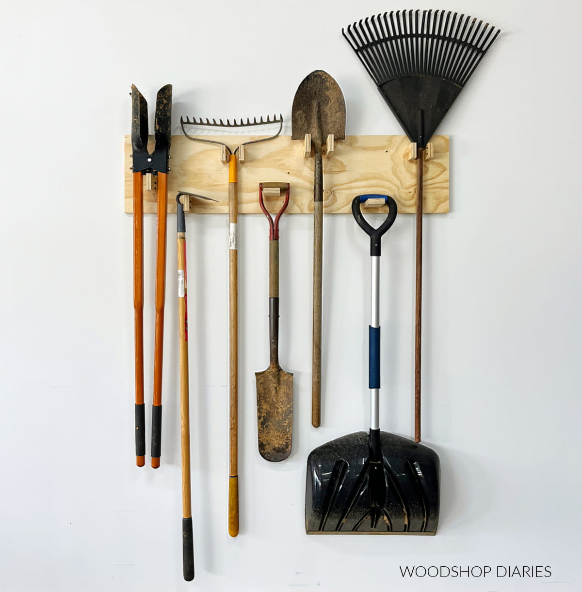 Garden tools hanging from a wall-mounted wood rack with simple wood pegs.