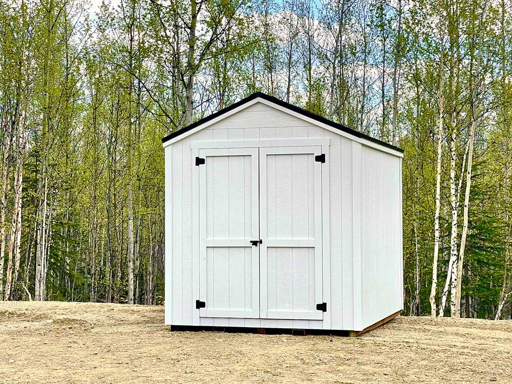 White double-door shed in front of a tree line