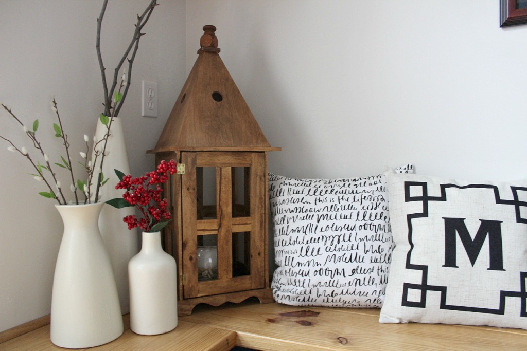 Wood lantern with a pitched roof and door next to vases and pillow