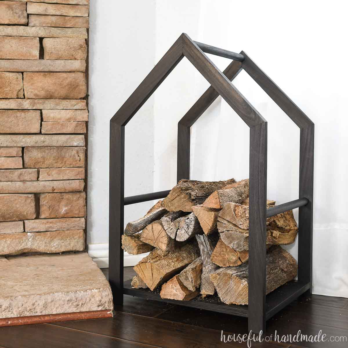 Brown-stained house-shaped firewood holder next to a hearth
