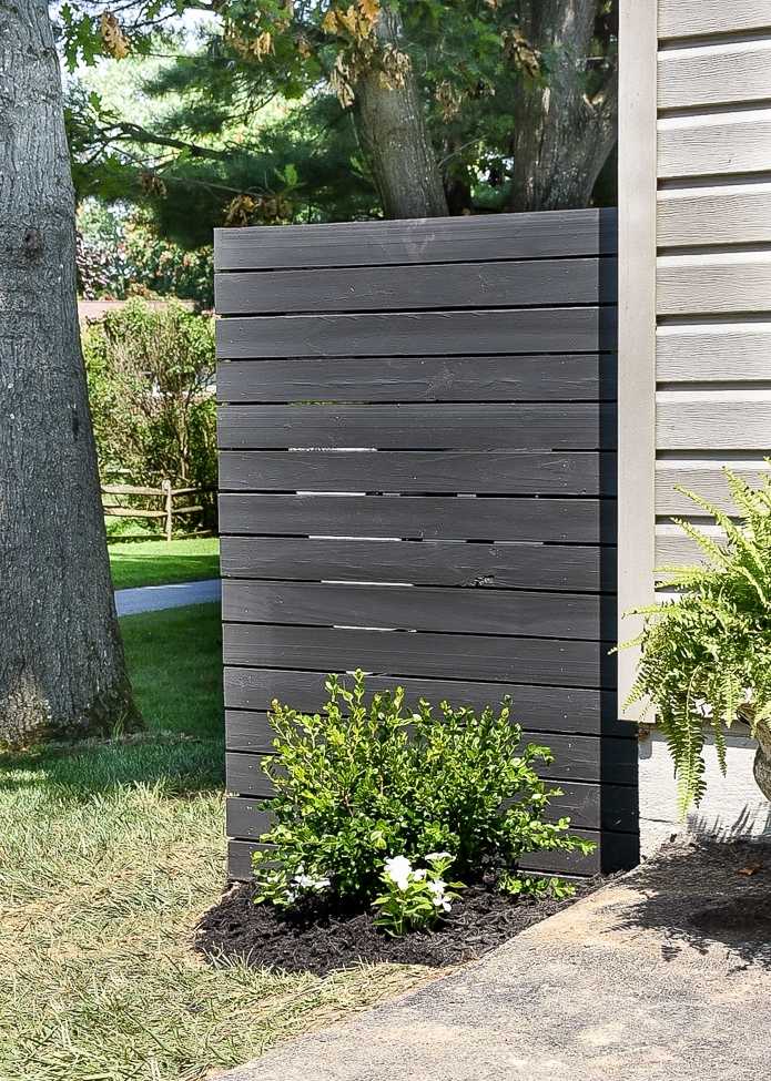 Horizontal slatted panel next to house for hiding garbage cans