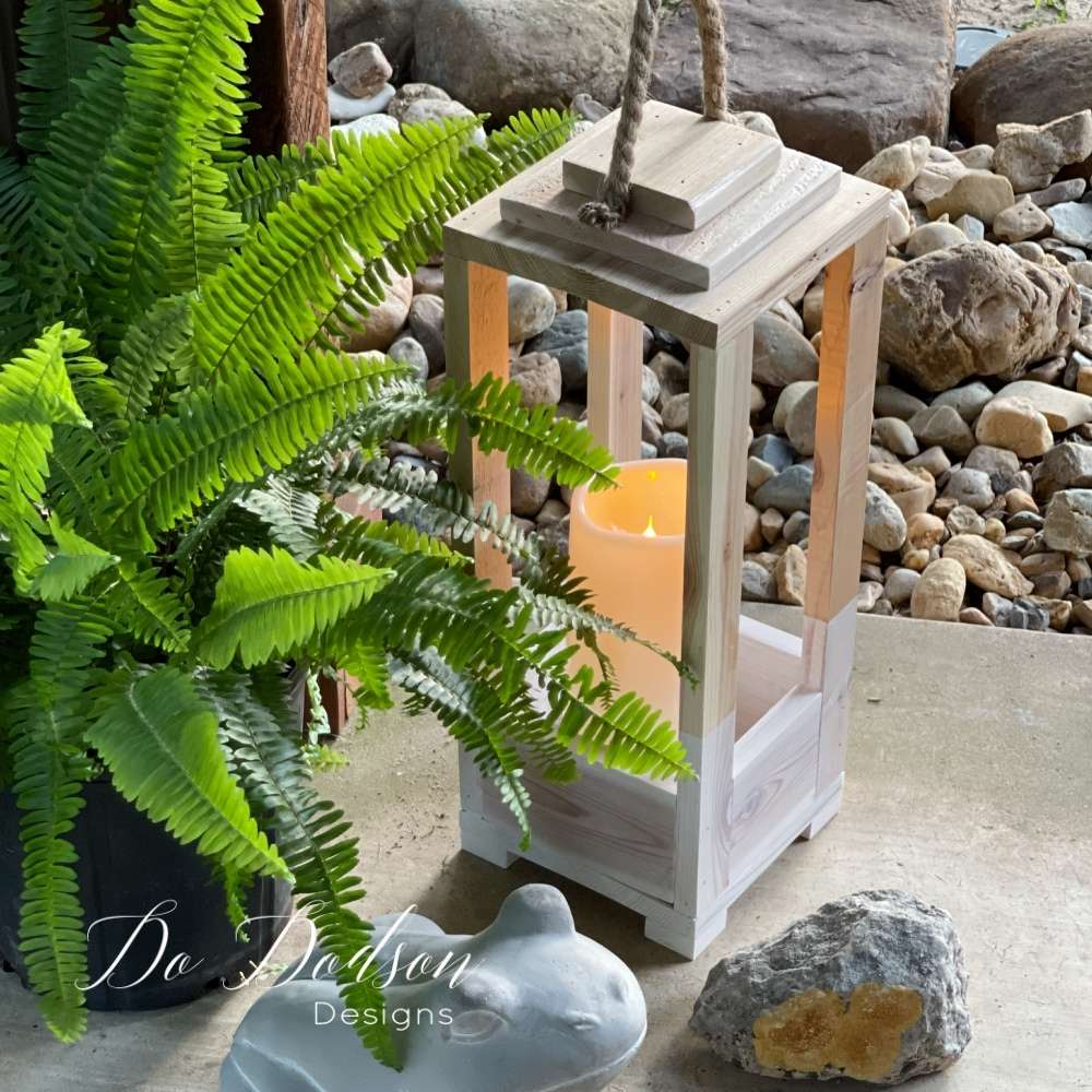 Wood lantern with a rope handle next to a fern
