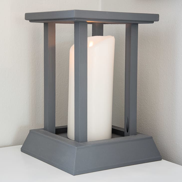 Gray painted wood lantern on a white table next to white wall