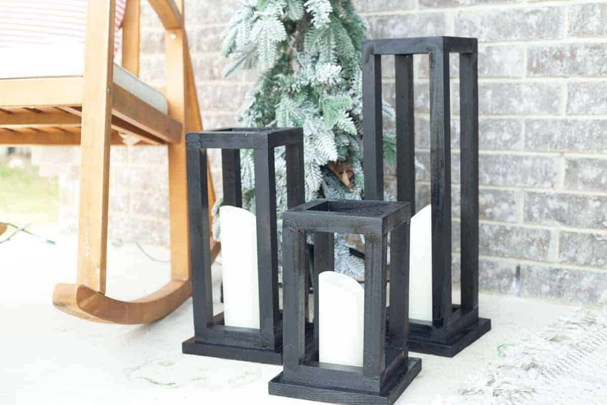 Three black painted wood lanterns in front of a light colored brick wall