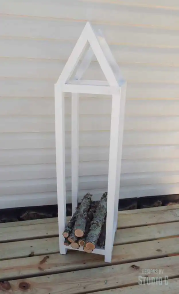 White-painted house-shaped log holder next to a house