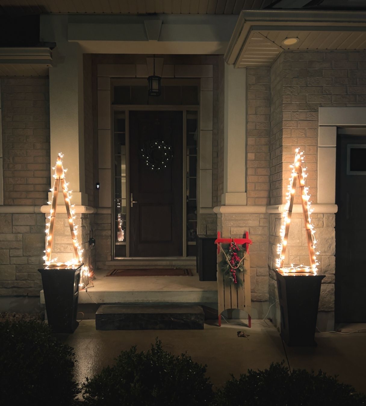 Two wooden outdoor Christmas trees on either side of an entry with white twinkle lights