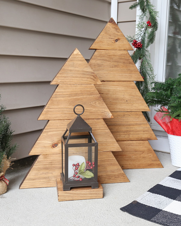 A pair of DIY wood Christmas trees, one with a lantern on a porch