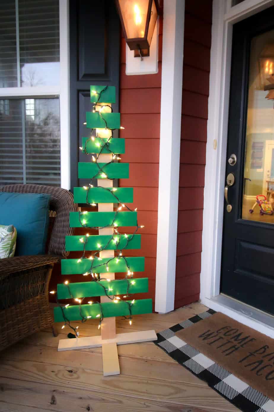 DIY outdoor wood Christmas tree with lights on a porch near a front door