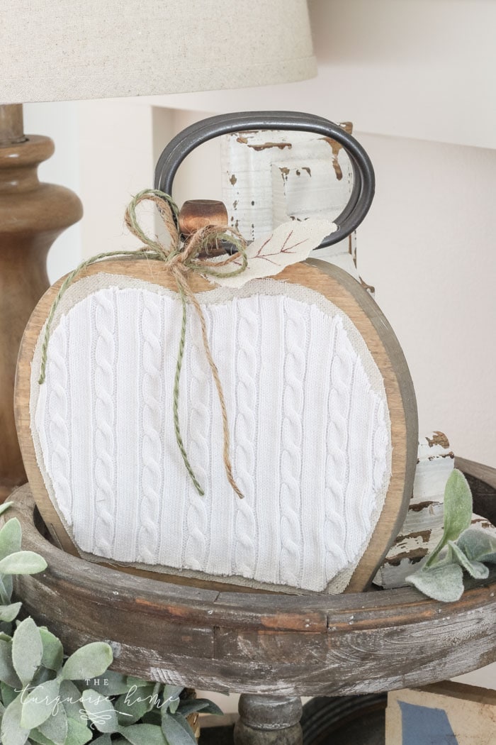 A wood board cut in the shape of a pumpkin and a white sweater-like material applied to the front