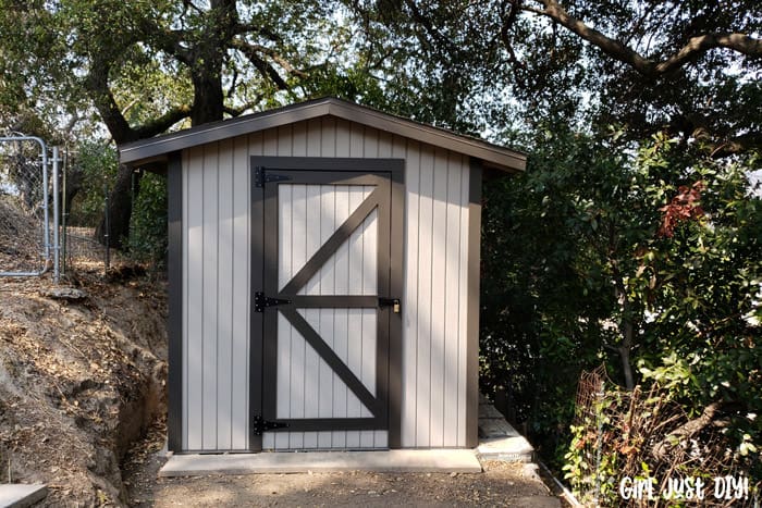 Two-tone gray shed on a concrete slab next to a hill