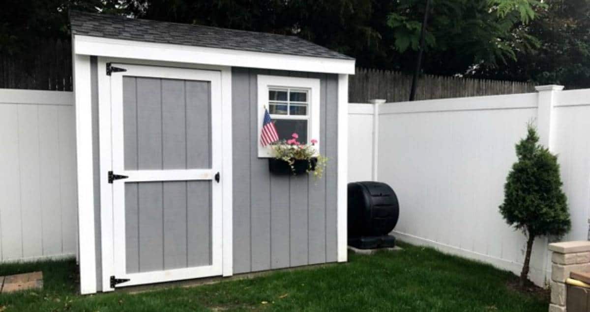 Gray shed with white trim next to a fence