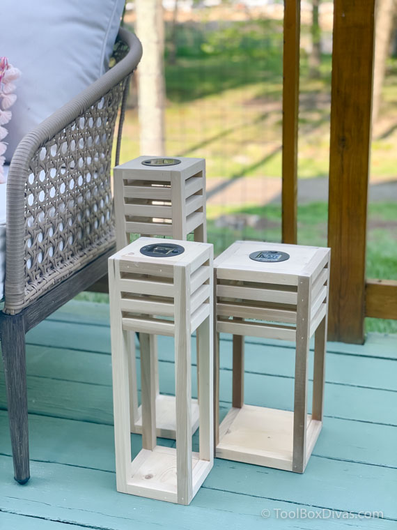 Three wood solar lanterns on a deck next to an outdoor couch