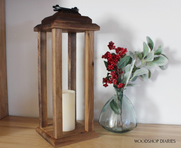 Tall wood lantern next to a vase with greenery