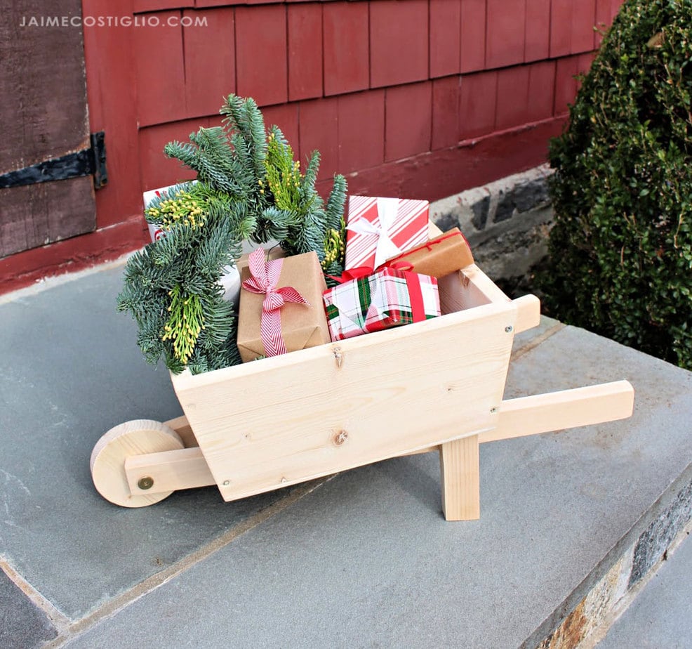 Natural wood wheelbarrow filled with greenery and gifts