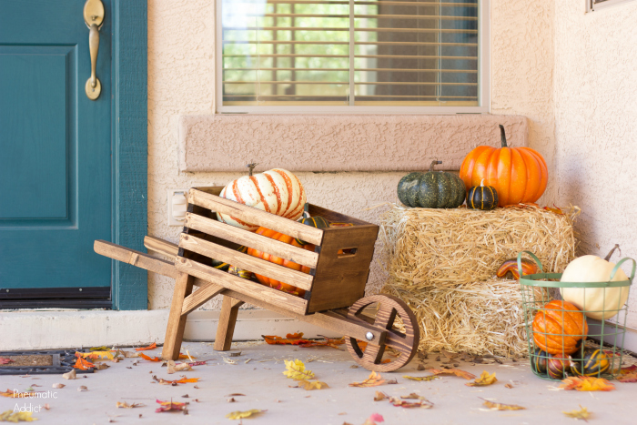 Wooden wheelbarrow on a porch with hay bales and pumpkins