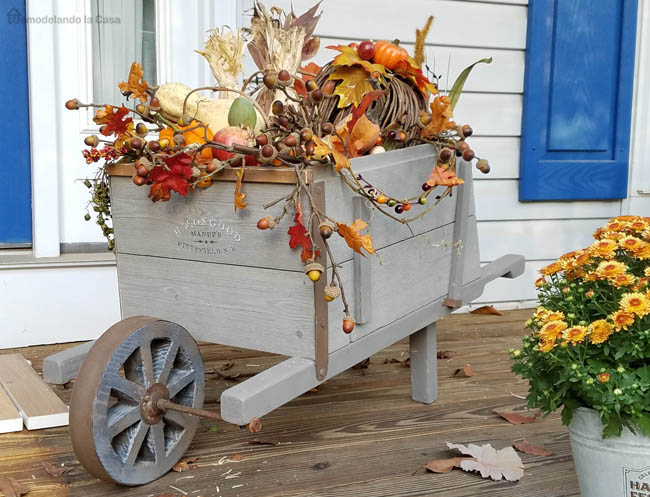 Gray wheelbarrow filled with fall decor on a porch