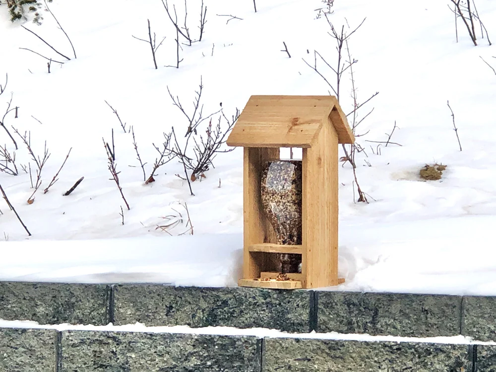 Wooden bird feeder on a stone wall with snow in the background