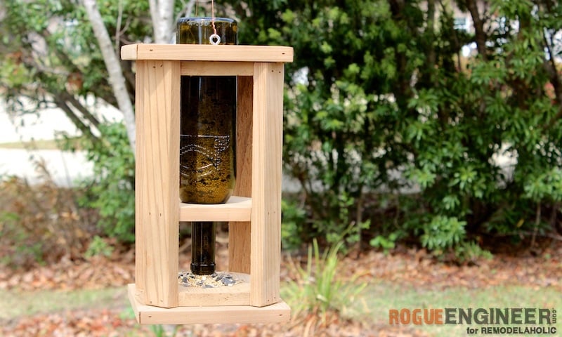Bird feeder with a wine bottle in the middle with trees in the background