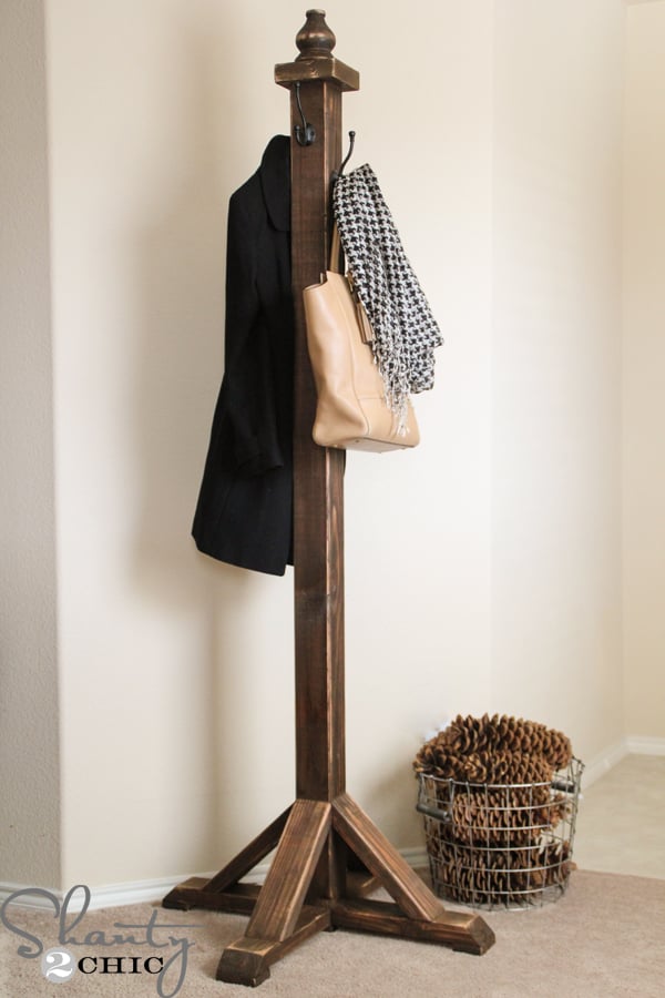 Free-standing coat rack with several coats and a bucket of pine cones at the base