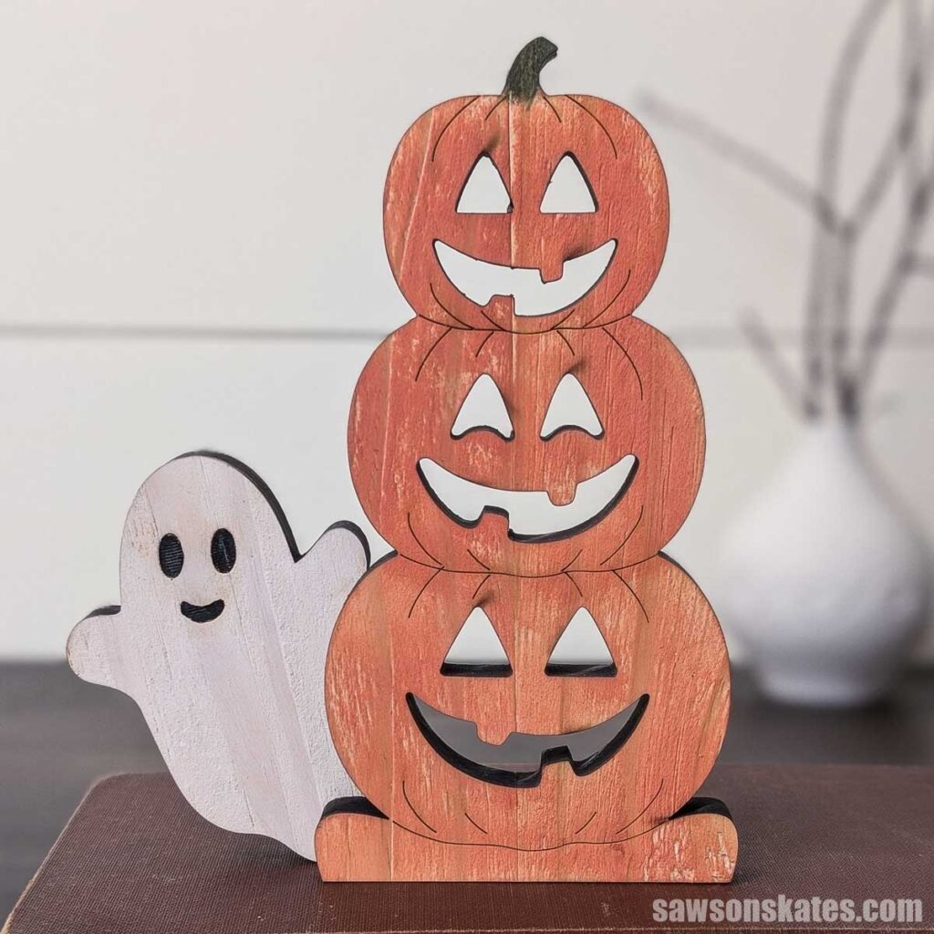 Front view of wooden stacked jack-o-lanterns with a ghost sitting on books