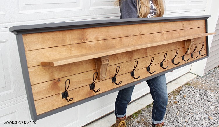 Person holding a long coat rack with a shelf and ten hooks below