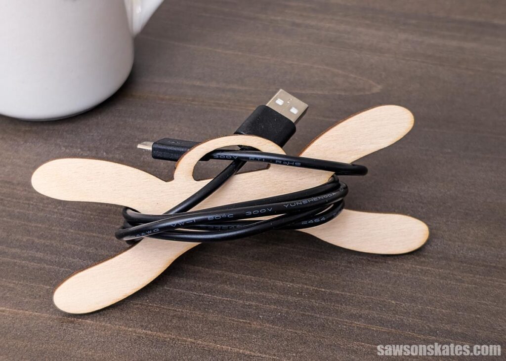 Wooden cord organizer with a black charging cable on a tabletop.