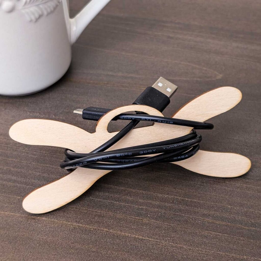 Wooden cord organizer with a black charging cable on a tabletop.