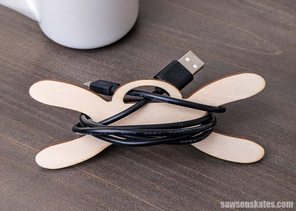 Front view of a wood cord organizer with a black charging cable on a tabletop.