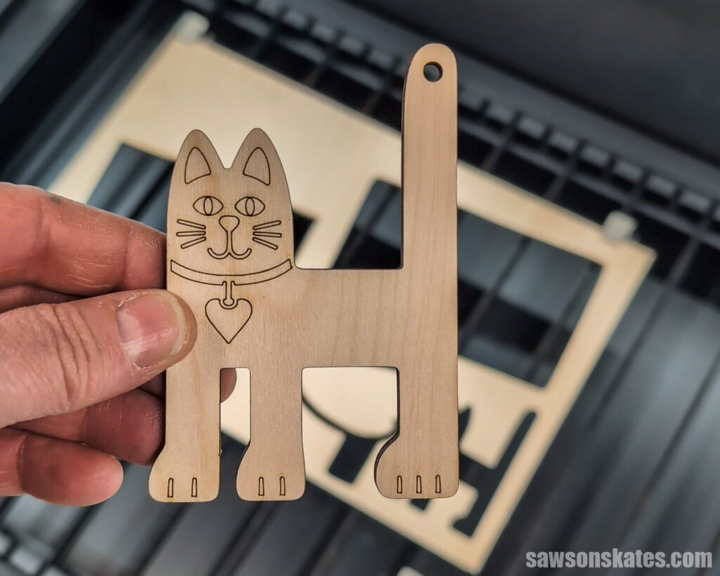 Scott holding holding a wooden cat cutout above a laser cutter