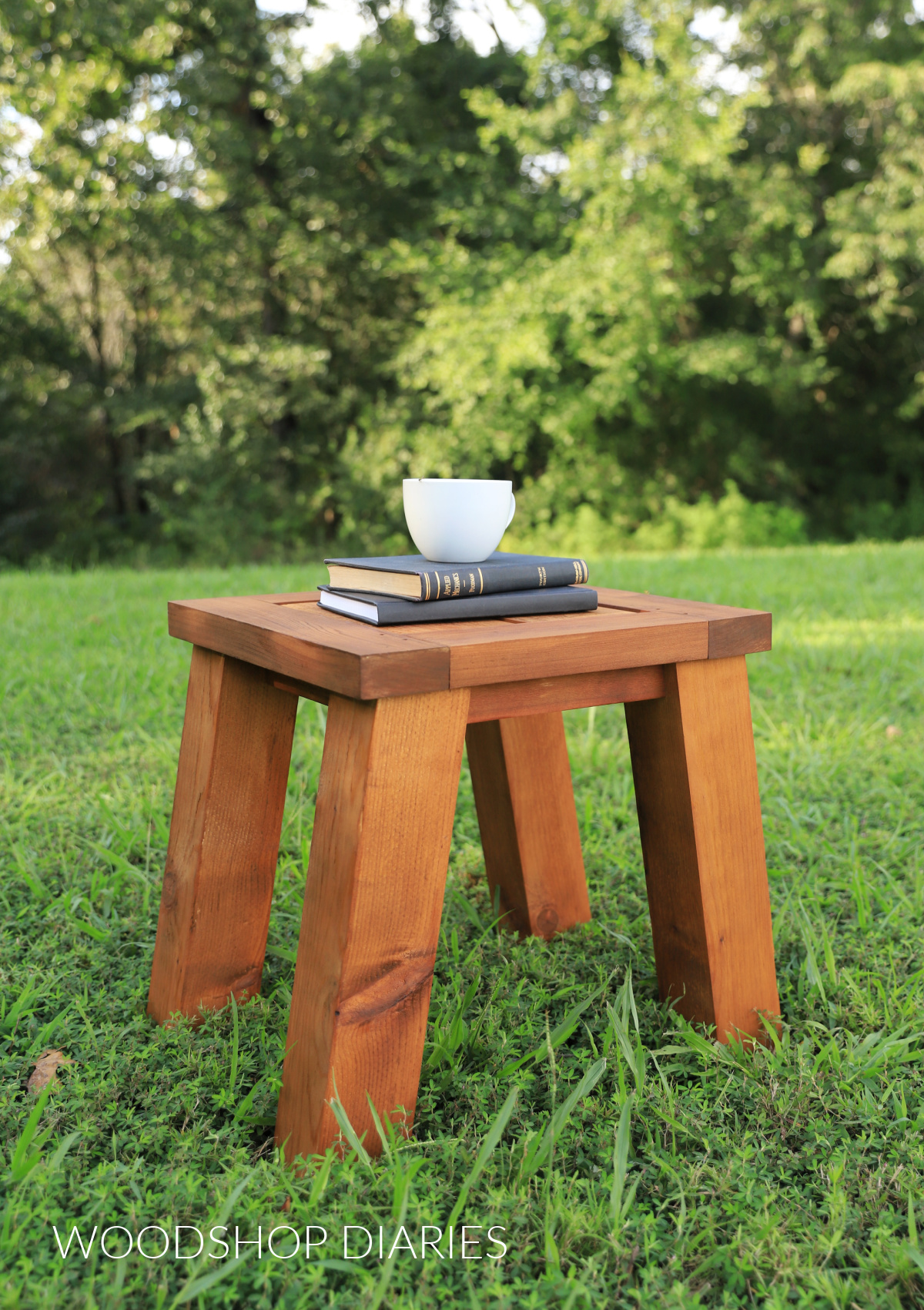 Small wooden outdoor side table with angled legs sitting on a grassy lawn.