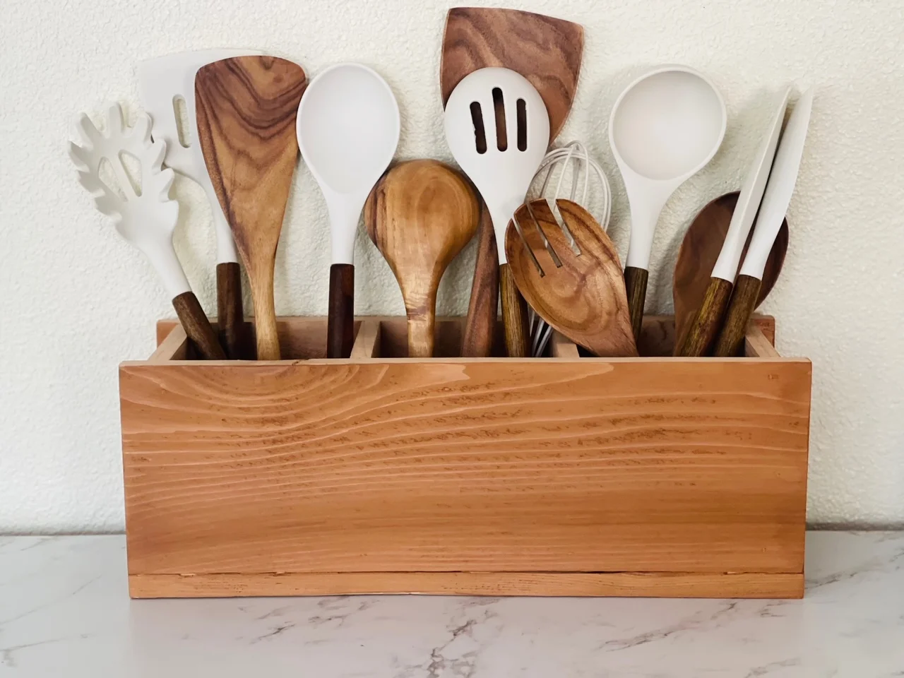 Wooden kitchen utensil holder filled with wood and white silicone cooking utensils.