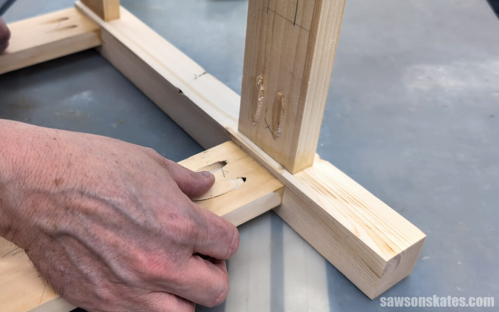 Close-up of a hand pressing a wooden pocket hole plug into a pocket hole on a woodworking project. The unfinished wood frame is resting on a workbench during assembly.