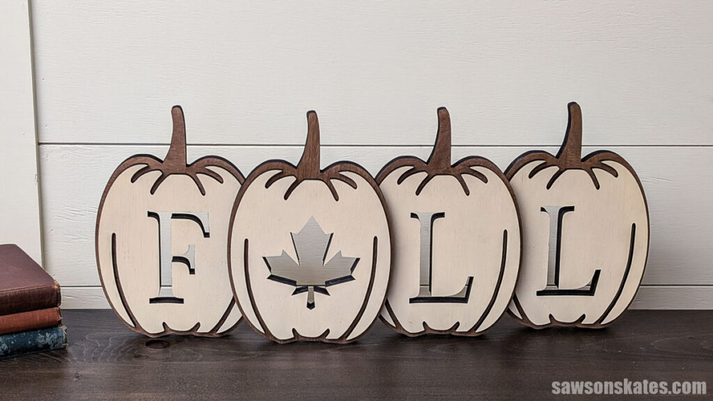 Front view of a layered pumpkin fall sign on a dark table next to a stack of books