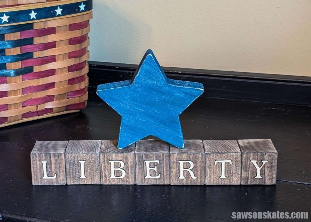 Handmade patriotic wood block decoration featuring stained wooden blocks that spell ‘LIBERTY’ with a blue painted wooden star centered above the letters.