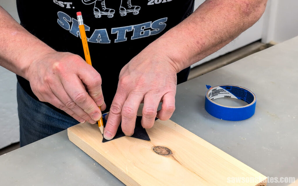 Person using a pencil and star-shaped template to trace a star onto a pine board.