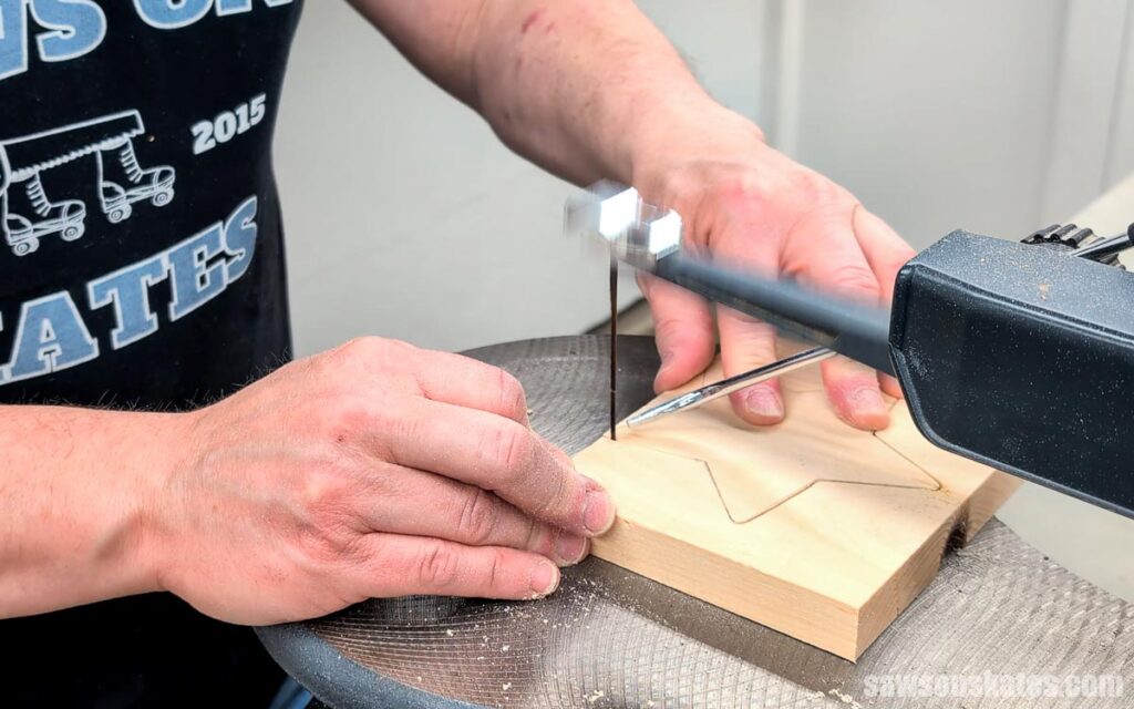 Person cutting a star shape from a pine board on a scroll saw.