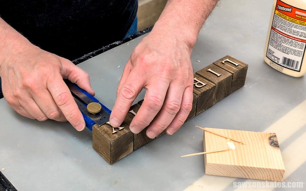 Hands positioning wooden letters on stained wood blocks.