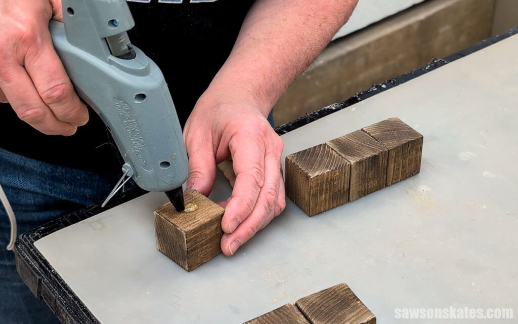 Person applying hot glue to the top of a stained wood block.