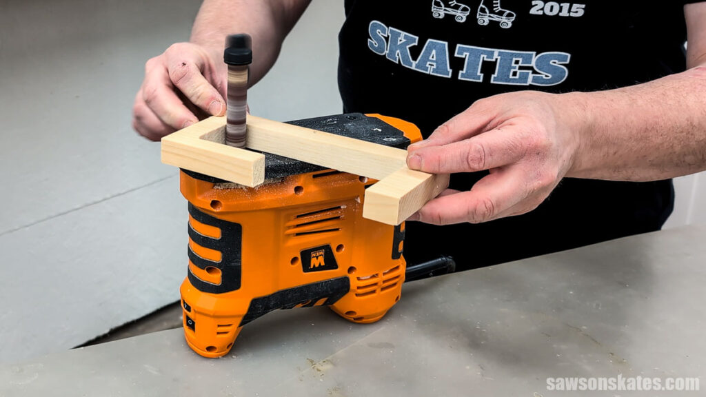 Hands sanding the inside edge of a U-shaped wooden piece using a spindle sand