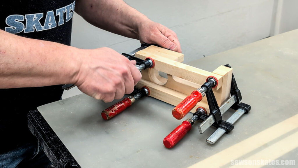 Hands tightening clamps around glued wooden pieces on a work surface.