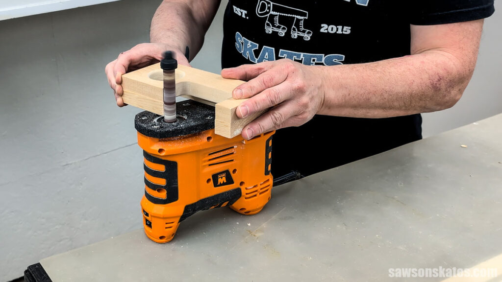 Hands sanding the edge of a glued wooden assembly on a portable spindle sander to make the pieces flush.