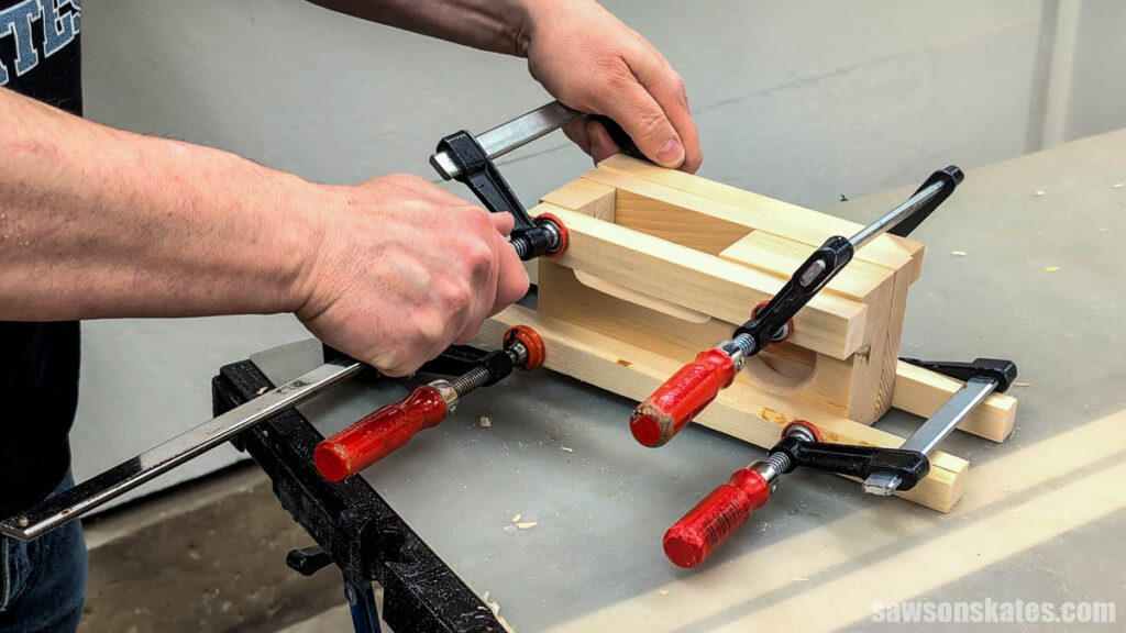 Hands tightening multiple clamps around a glued wooden assembly to secure the pieces while drying.