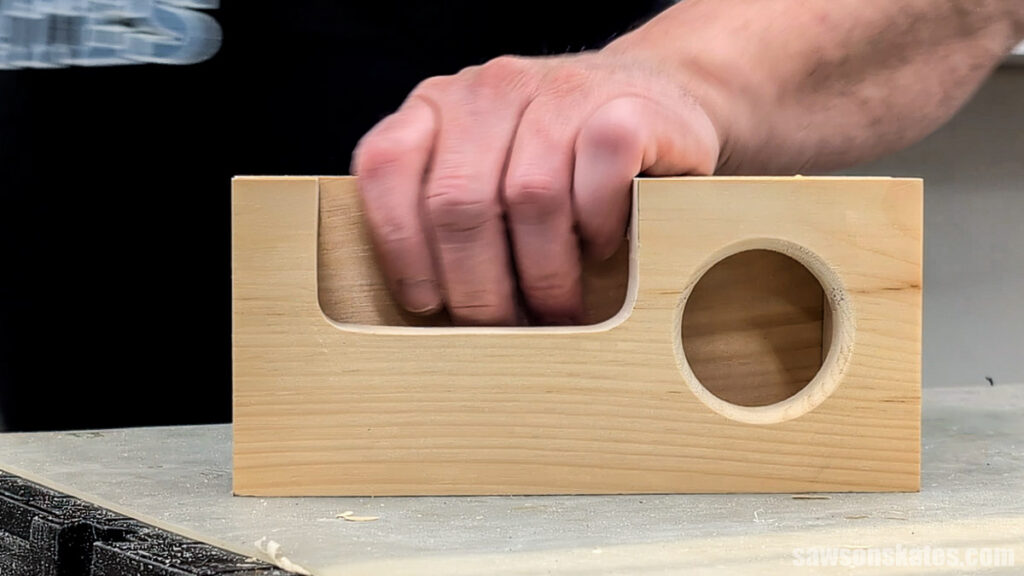 Hand holding the rectangular phone slot in a wooden phone amplifier with a round speaker opening.