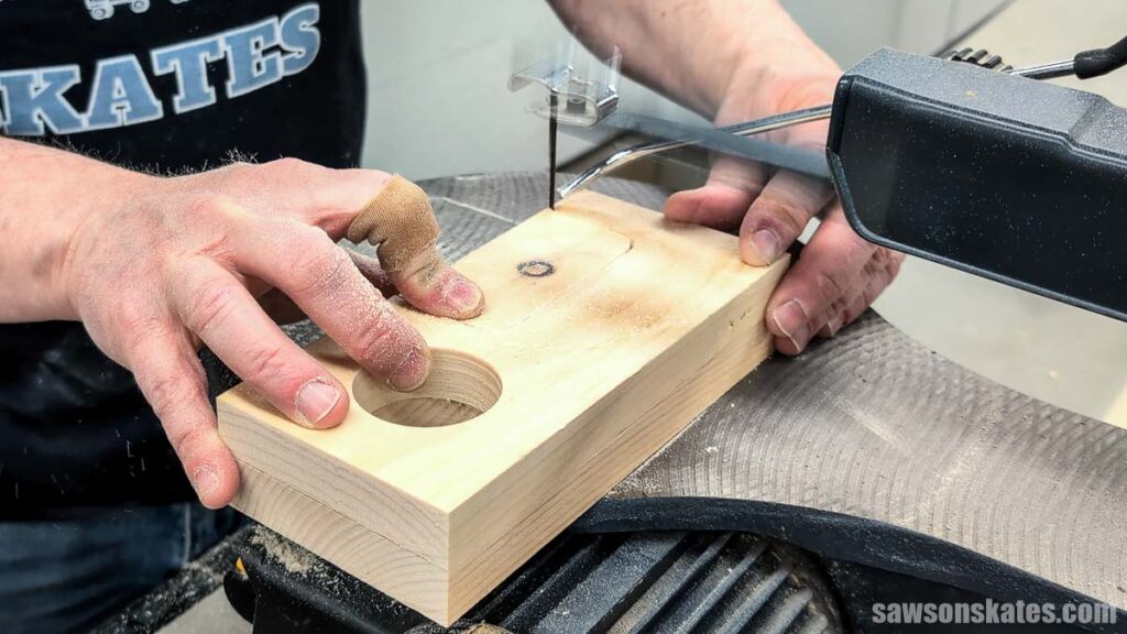Hands cutting a curved opening in a wood block with a scroll saw