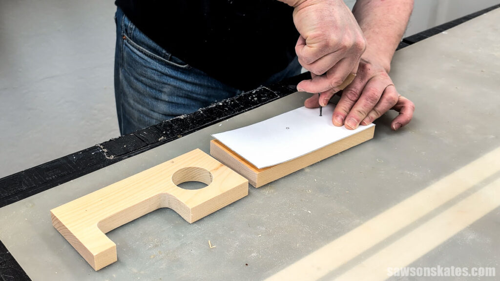 Hands marking a small wood block with an awl through a paper template