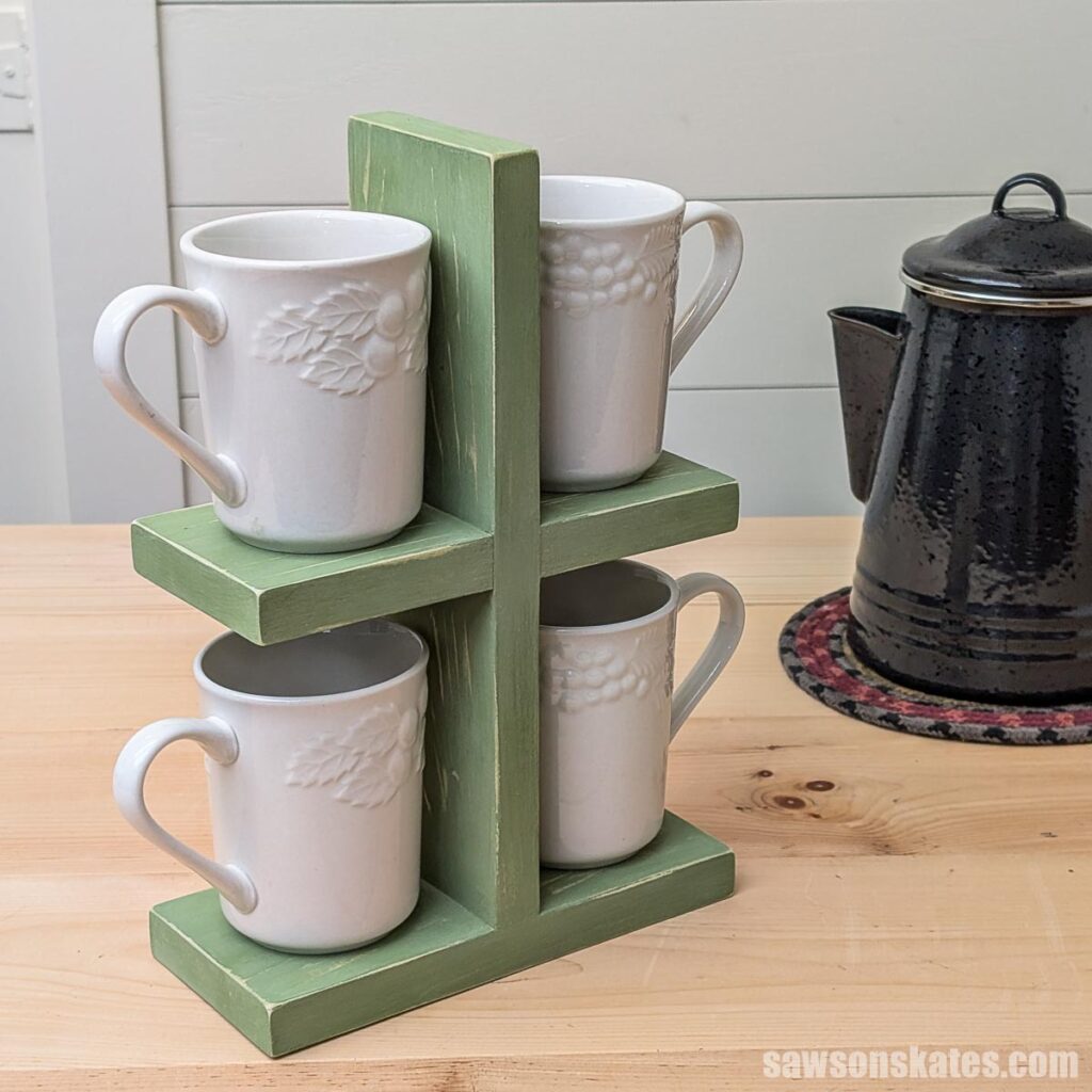 DIY stacked mug stand painted green with a distressed finish, holding four white mugs on a wood counter beside a black coffee pot